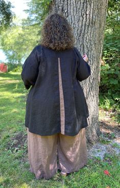 a woman standing in front of a tree with her back turned to the camera, wearing a black jacket and khaki pants