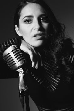 black and white photograph of a woman holding a microphone in front of her face, looking at the camera