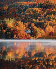 a lake surrounded by lots of trees with autumn foliage around it and a house in the distance