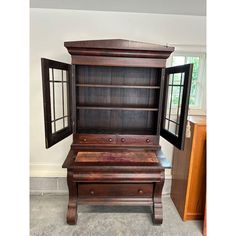 an old wooden desk with two open doors on the top and bottom, in front of a window