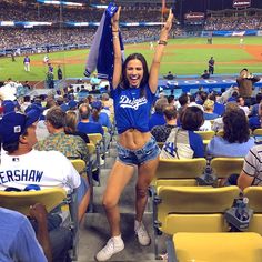 a woman in blue shirt and shorts standing on top of a baseball field with her arms up