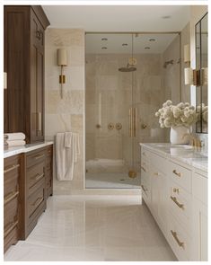 a bathroom with marble counter tops and gold accents on the shower door, along with white cabinets