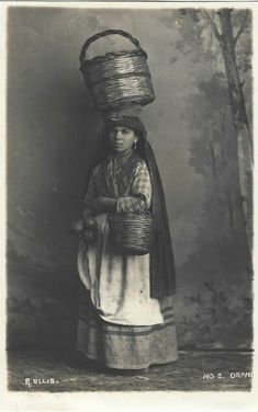 an old black and white photo of a woman with baskets on her head