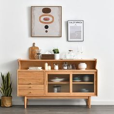 a wooden cabinet sitting next to a painting and potted plant on top of a hard wood floor