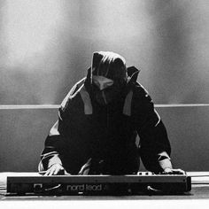 a person sitting on the ground in front of a laptop computer with their face covered by a hood