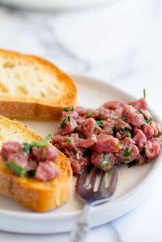 a white plate topped with bread and meat next to a fork on top of a table