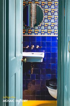 an open door leading to a bathroom with blue and yellow tiles on the walls, toilet and sink