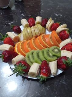 a plate filled with sliced up fruit on top of a marble countertop next to strawberries, oranges and kiwi