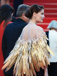 the back of a woman's dress with large feathers on it and people in the background