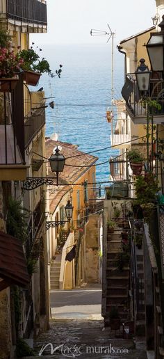 an alley way leading to the ocean with stairs going up and down in between two buildings