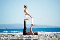 a woman doing yoga on the beach with her legs in the air while another person holds up their leg