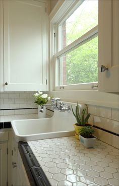 a white kitchen sink sitting under a window next to a potted plant on top of a counter