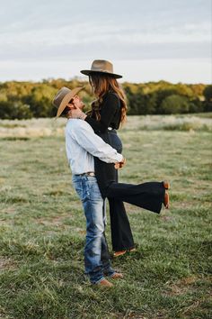 a pregnant woman is holding her husband's back in the middle of a field