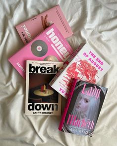 there are many books on the bed with white sheets and pink covers, including one that reads break down