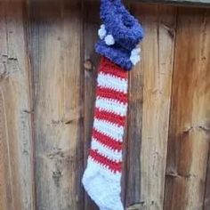 a red white and blue knitted christmas stocking hanging on a wooden fence post