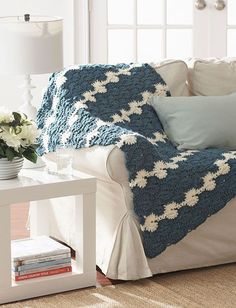 a blue and white crocheted afghan sitting on top of a couch next to a table