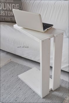 a laptop computer sitting on top of a white table next to a bed with pillows