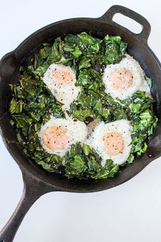 three fried eggs on top of greens in a cast iron skillet