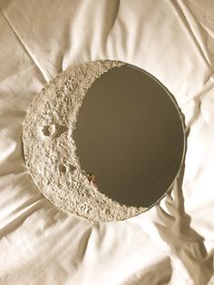 a mirror that is sitting on top of a white bed sheet with the moon in it's center