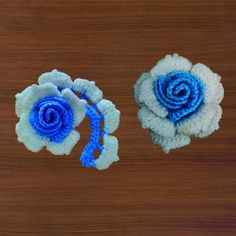 two crocheted blue and white flowers sitting on top of a wooden table next to each other