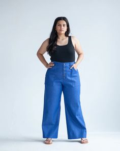 a woman standing in front of a white background wearing blue pants and a black tank top