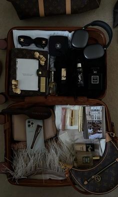 an open suitcase filled with personal items on top of a floor next to a handbag