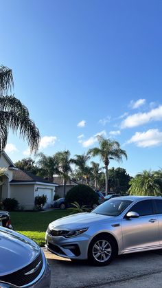 two cars parked in front of a house on a street with palm trees behind them