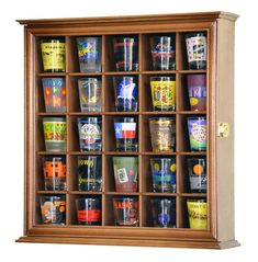 a wooden case filled with lots of different types of shot glasses on top of a white wall