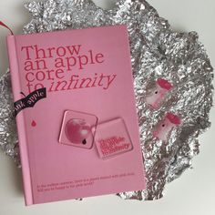 a pink book sitting on top of a piece of tin foil next to an apple