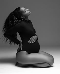 a pregnant woman sitting on the floor with her hands behind her back and looking up