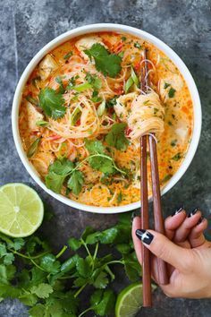 someone is holding chopsticks over a bowl of noodles and cilantro sauce