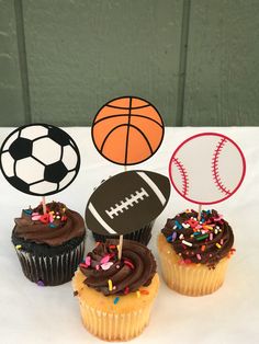 three cupcakes with chocolate frosting and sports balls on top are sitting on a table