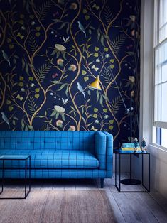 a blue couch sitting in front of a wallpapered room with birds on it