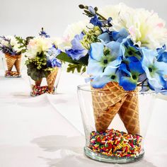 three ice cream cones with flowers and sprinkles in them on a table