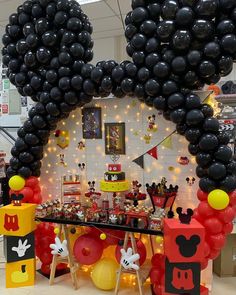 a mickey mouse balloon arch is decorated with black and red balloons, yellow and orange decorations