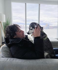 a man sitting on top of a couch next to a husky dog in his lap