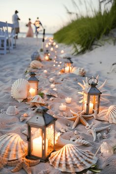 candles are lined up on the sand near shells and seashells