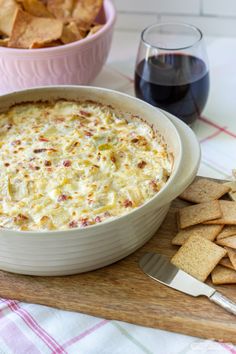 a bowl of dip next to some crackers and a glass of wine