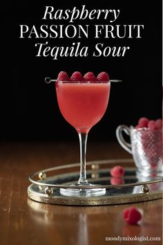 raspberry passion fruit tequila sour in a coupe glass on a tray with raspberries