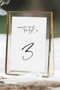 a table number is placed in a gold frame on top of a white table cloth