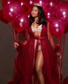 a woman wearing a red gown and crown standing in front of balloons with her hands on her hips