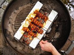 someone is cooking food on the grill with skewered meats and sauce over it