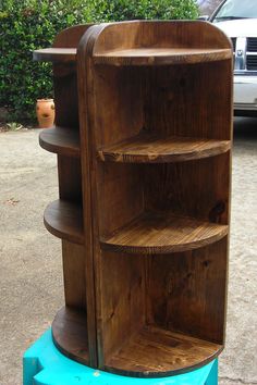 a wooden book shelf sitting on top of a blue plastic container next to a tree