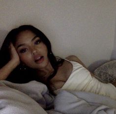 a woman laying on top of a bed covered in white sheets and blankets with her hand under her head