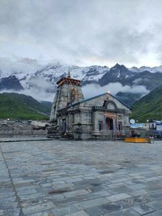 an old building in the middle of a mountain range with snow capped mountains behind it