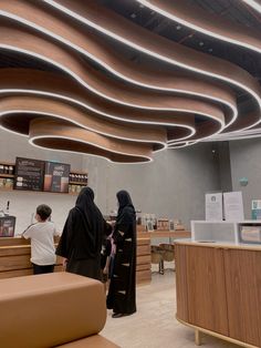 two women are standing in front of a counter at a coffee shop with wooden furniture