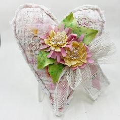 a heart shaped box with flowers and lace on it's sides sitting on a white surface