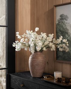 a vase filled with white flowers sitting on top of a table next to a painting