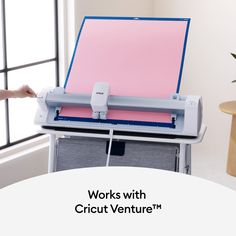 a person is using a machine to cut paper with a pink sheet on the table