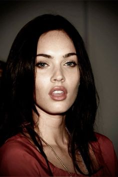 a woman with long dark hair and blue eyes is posing for the camera, wearing a red top